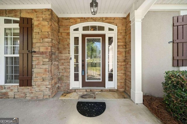 view of exterior entry featuring stone siding, covered porch, and stucco siding