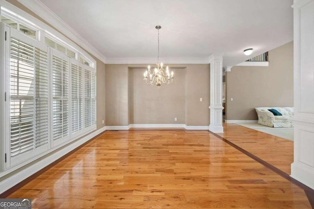 unfurnished dining area featuring light wood-style flooring, baseboards, a chandelier, ornate columns, and crown molding