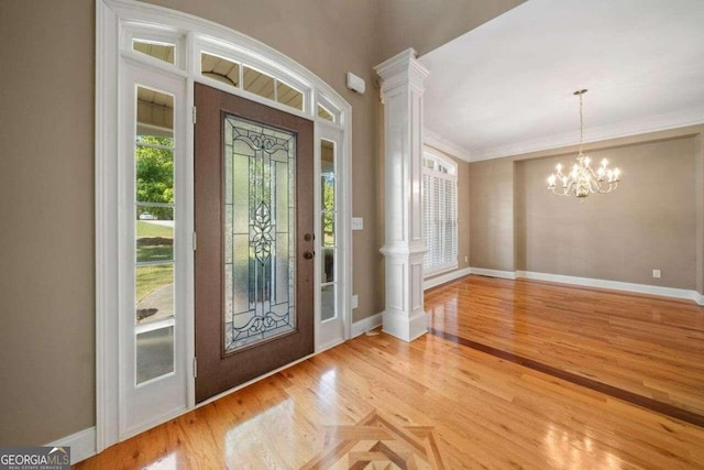 foyer entrance featuring ornate columns, plenty of natural light, ornamental molding, and an inviting chandelier