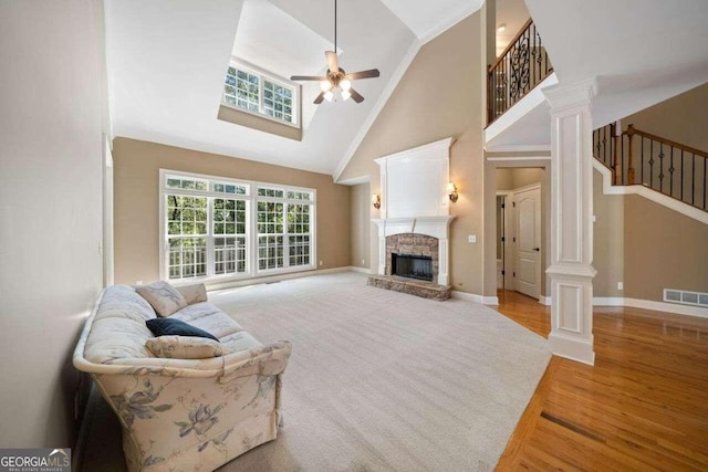 living room with ceiling fan, high vaulted ceiling, a fireplace, decorative columns, and light wood-type flooring