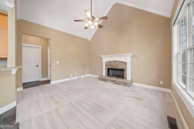 unfurnished living room with ceiling fan, dark carpet, a stone fireplace, high vaulted ceiling, and crown molding