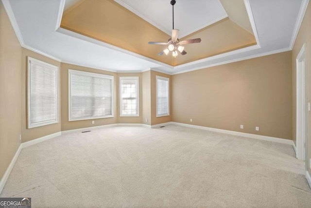 carpeted spare room with ceiling fan, baseboards, ornamental molding, and a raised ceiling