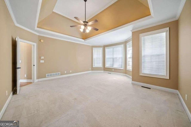 empty room featuring ornamental molding, light colored carpet, ceiling fan, and a raised ceiling