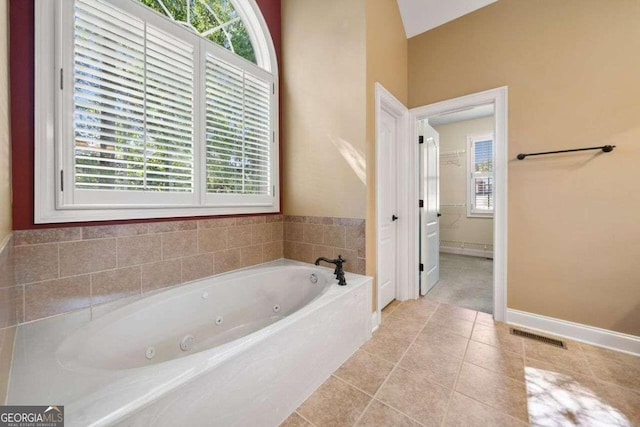 bathroom with vaulted ceiling, a tub to relax in, plenty of natural light, and tile patterned flooring