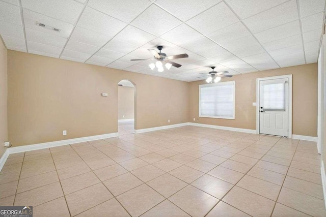 empty room with visible vents, arched walkways, light tile patterned flooring, a paneled ceiling, and ceiling fan