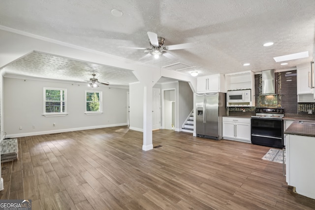 kitchen with white appliances, wall chimney range hood, a textured ceiling, hardwood / wood-style floors, and white cabinetry