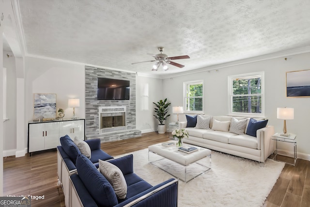 living room with a stone fireplace, a textured ceiling, ornamental molding, and dark hardwood / wood-style floors