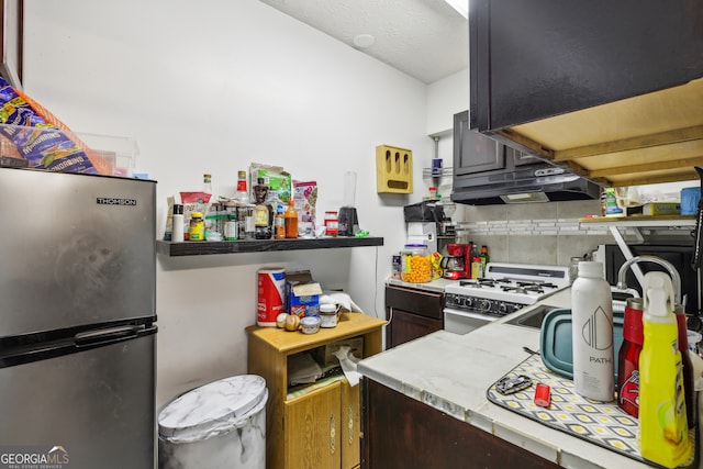 kitchen featuring white range with gas stovetop, decorative backsplash, and stainless steel refrigerator