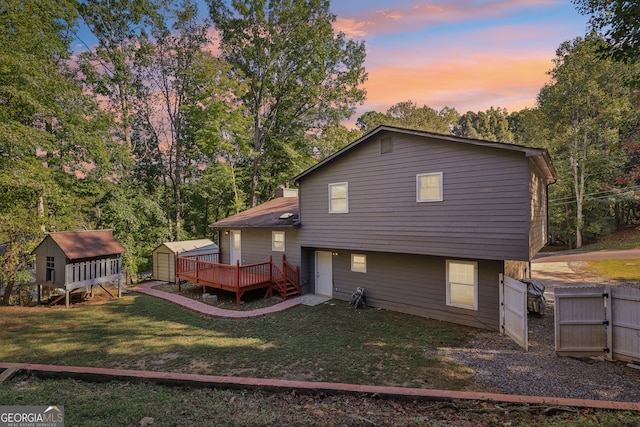 back house at dusk featuring a shed, a deck, and a lawn