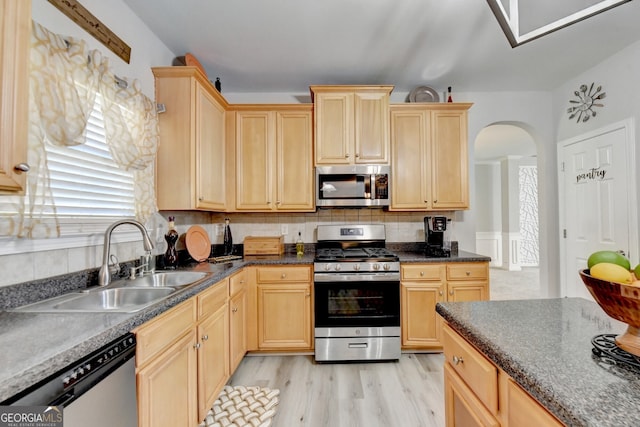 kitchen with decorative backsplash, appliances with stainless steel finishes, light brown cabinetry, sink, and light hardwood / wood-style flooring