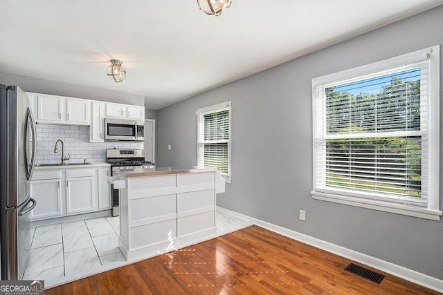 kitchen featuring light wood-type flooring, tasteful backsplash, stainless steel appliances, sink, and white cabinetry