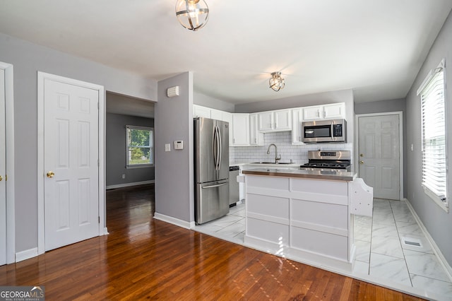 kitchen with white cabinetry, sink, stainless steel appliances, backsplash, and light wood-type flooring