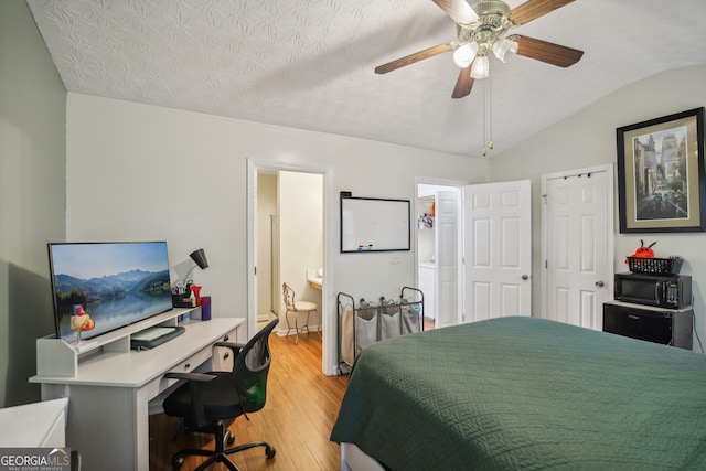 bedroom with ceiling fan, light hardwood / wood-style floors, ensuite bath, vaulted ceiling, and a textured ceiling