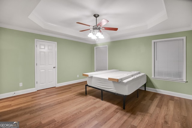 bedroom featuring light wood-type flooring, a tray ceiling, ceiling fan, and crown molding