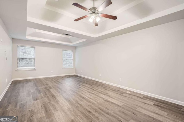 empty room with ceiling fan, a raised ceiling, and wood-type flooring