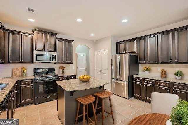 kitchen featuring black appliances, decorative backsplash, a kitchen island, and dark brown cabinets