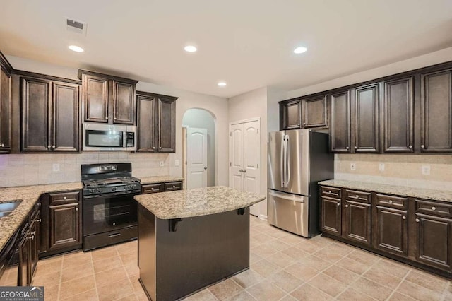 kitchen with a center island, black appliances, decorative backsplash, light stone countertops, and dark brown cabinets