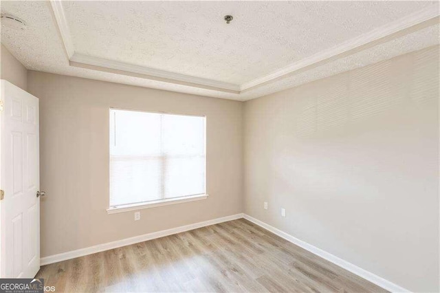 unfurnished room featuring a textured ceiling, light hardwood / wood-style flooring, and a raised ceiling