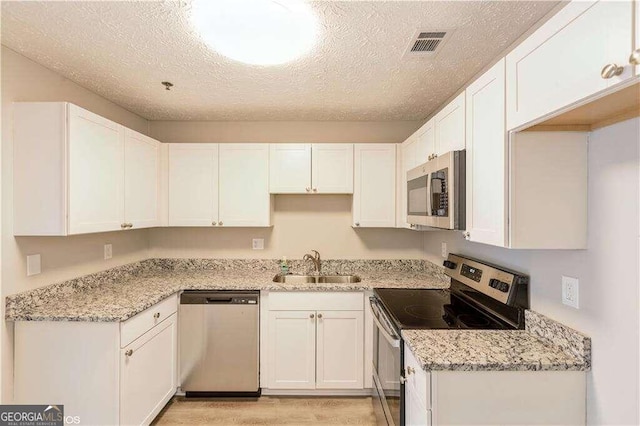 kitchen with sink, light stone counters, white cabinets, appliances with stainless steel finishes, and a textured ceiling