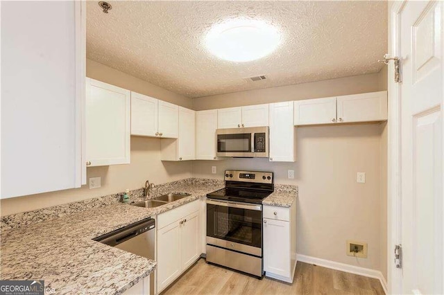 kitchen featuring light stone counters, white cabinets, sink, stainless steel appliances, and light hardwood / wood-style floors