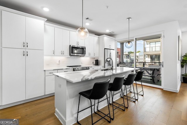 kitchen featuring white cabinets, pendant lighting, wood-type flooring, a center island with sink, and appliances with stainless steel finishes