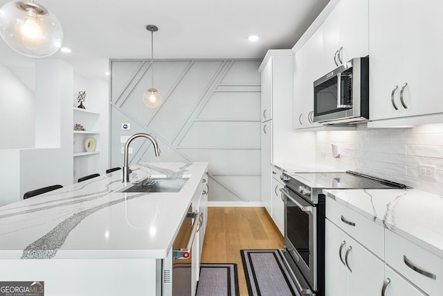 kitchen with white cabinets, an island with sink, sink, stainless steel appliances, and light hardwood / wood-style floors