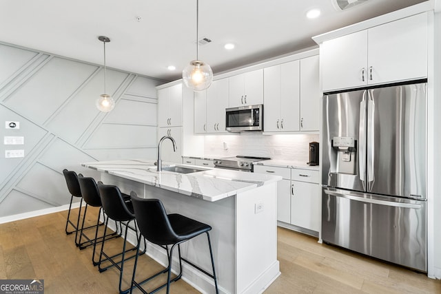 kitchen with stainless steel appliances, white cabinets, hanging light fixtures, light hardwood / wood-style flooring, and a center island with sink