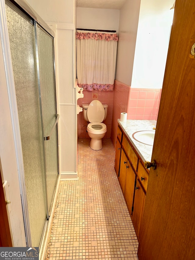 bathroom featuring toilet, walk in shower, vanity, and tile walls