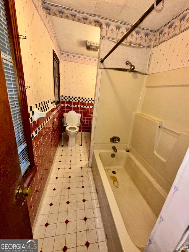 bathroom with tile walls, bathtub / shower combination, and toilet