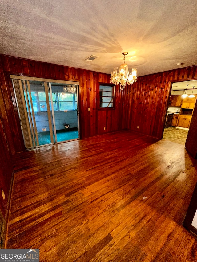 interior space with hardwood / wood-style flooring, wooden walls, an inviting chandelier, and a textured ceiling