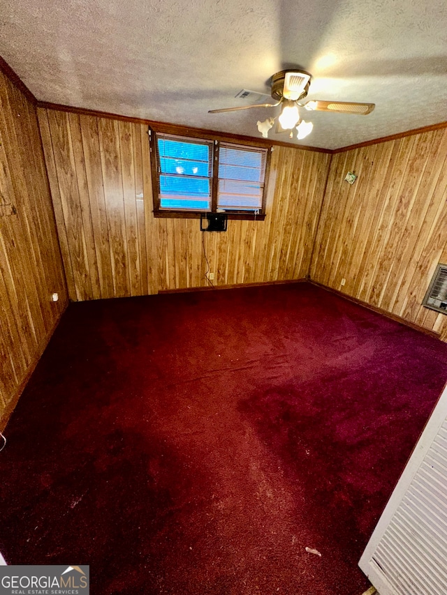 empty room featuring ceiling fan, wood walls, and a textured ceiling