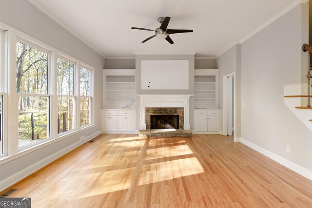 unfurnished living room with a stone fireplace, ceiling fan, built in features, and light wood-type flooring