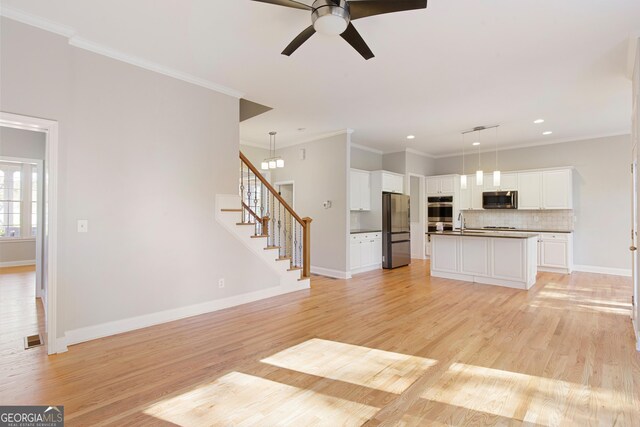 kitchen featuring backsplash, a center island with sink, hanging light fixtures, appliances with stainless steel finishes, and white cabinetry