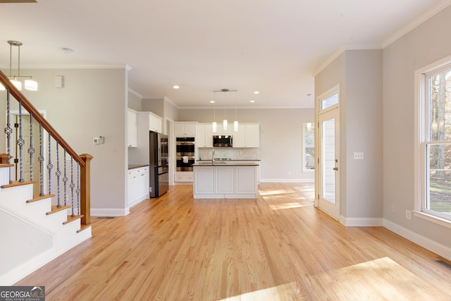 kitchen with pendant lighting, white cabinets, stainless steel appliances, and a center island with sink