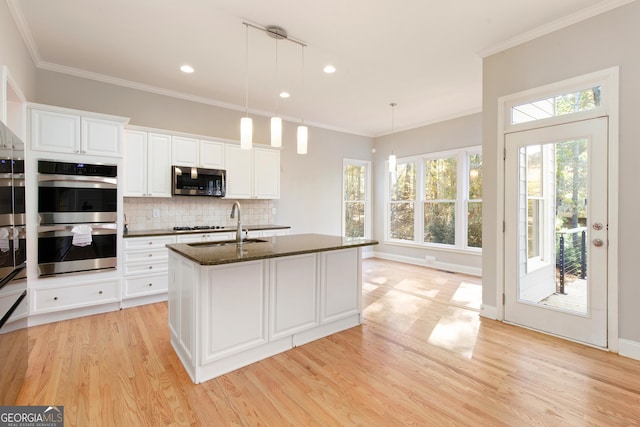 kitchen with white cabinetry, dark stone counters, pendant lighting, a center island with sink, and appliances with stainless steel finishes