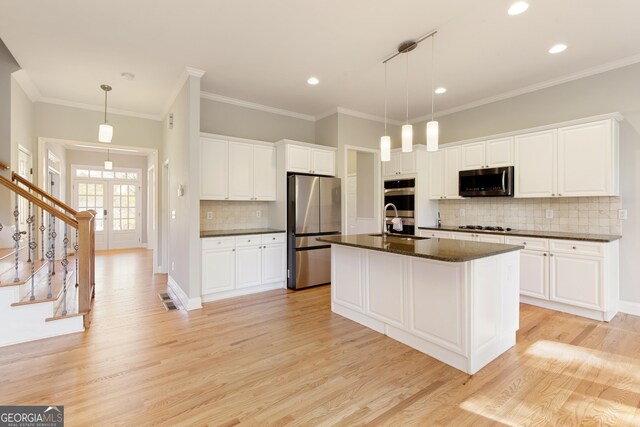 kitchen with stainless steel appliances, pendant lighting, a center island with sink, light hardwood / wood-style floors, and white cabinetry