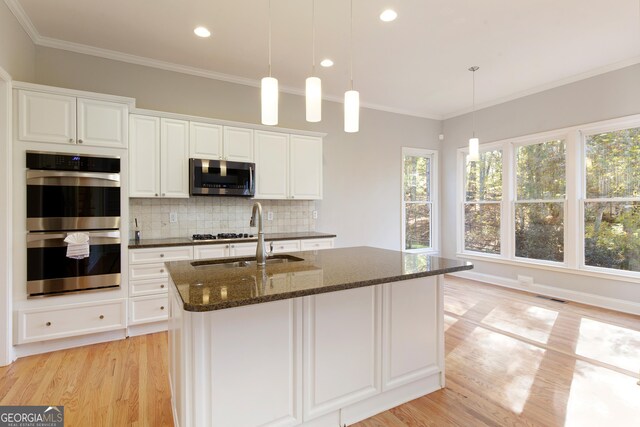 kitchen featuring white cabinetry, sink, stainless steel appliances, dark stone counters, and a center island with sink