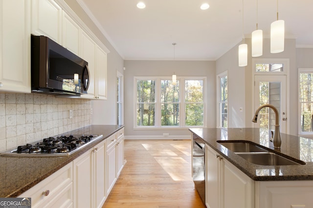 kitchen featuring sink, dark stone countertops, an island with sink, appliances with stainless steel finishes, and ornamental molding