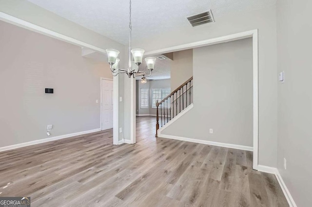 unfurnished dining area featuring a textured ceiling, light hardwood / wood-style floors, and a notable chandelier