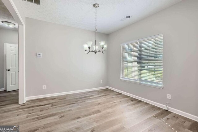 spare room with hardwood / wood-style floors, a textured ceiling, and an inviting chandelier