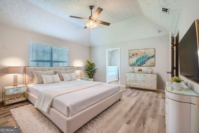 bedroom with light hardwood / wood-style flooring, vaulted ceiling, ceiling fan, a textured ceiling, and connected bathroom