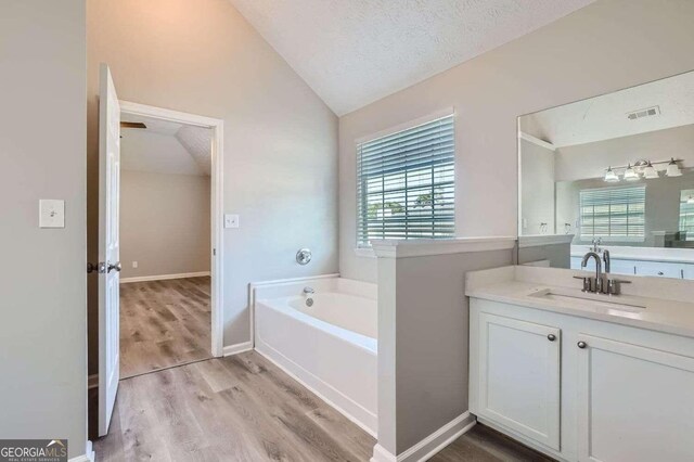 bathroom featuring a textured ceiling, a wealth of natural light, hardwood / wood-style floors, and lofted ceiling