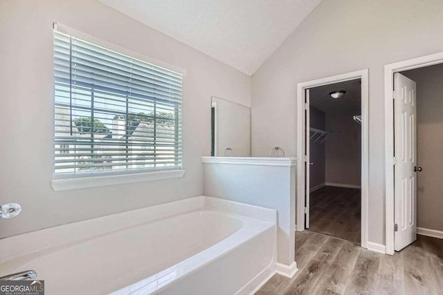 bathroom featuring a bath, wood-type flooring, a textured ceiling, and vaulted ceiling