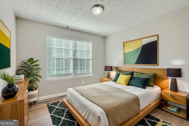 bedroom with a textured ceiling and light hardwood / wood-style flooring