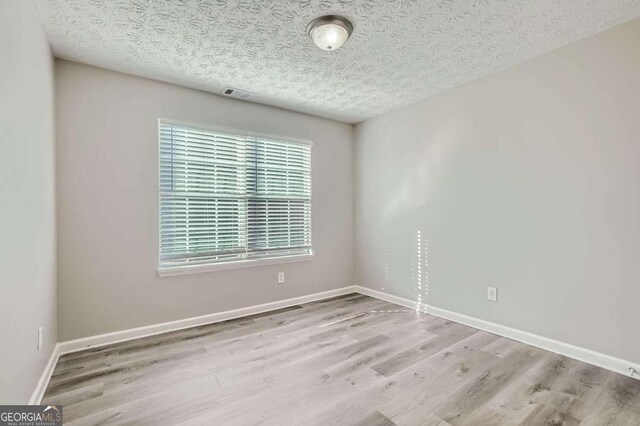 empty room featuring a textured ceiling and light hardwood / wood-style flooring