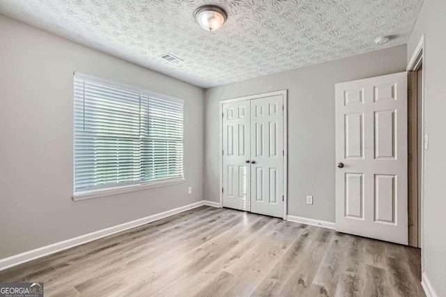 unfurnished bedroom with light hardwood / wood-style floors, a textured ceiling, and a closet