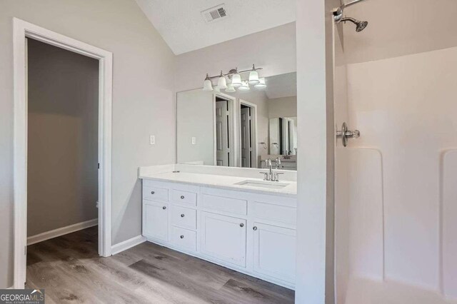 bathroom featuring hardwood / wood-style floors, vanity, a shower, and lofted ceiling