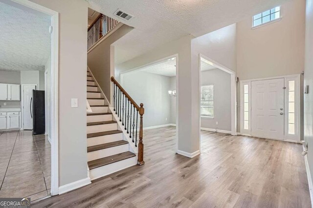 entrance foyer with a high ceiling, a textured ceiling, and light hardwood / wood-style flooring