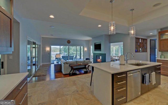 kitchen featuring light wood-type flooring, hanging light fixtures, sink, stainless steel dishwasher, and a kitchen island with sink