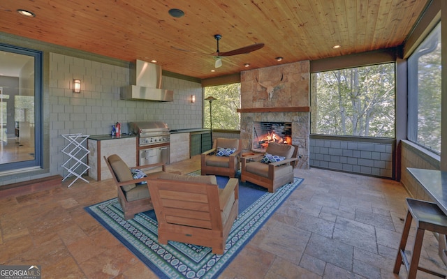 sunroom / solarium featuring ceiling fan, wood ceiling, and an outdoor stone fireplace